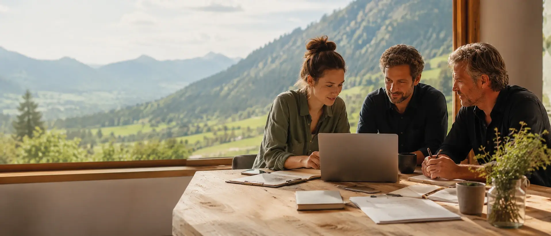 menschen pruefen gemeinsam eine informationsanfrage am laptop mit unterlagen auf einem holztisch und blick in die berge